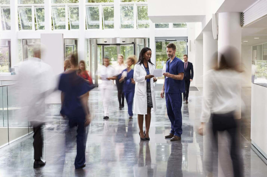 A male and female doctor reviewing a chart together in the middle of a busy hospital walkway area.