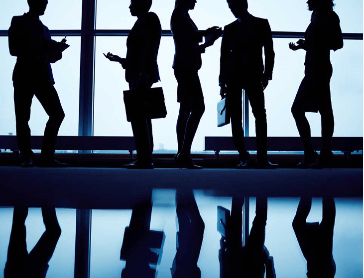 The silhouettes of 5 office employees holding suitcases and talking amongst themselves.