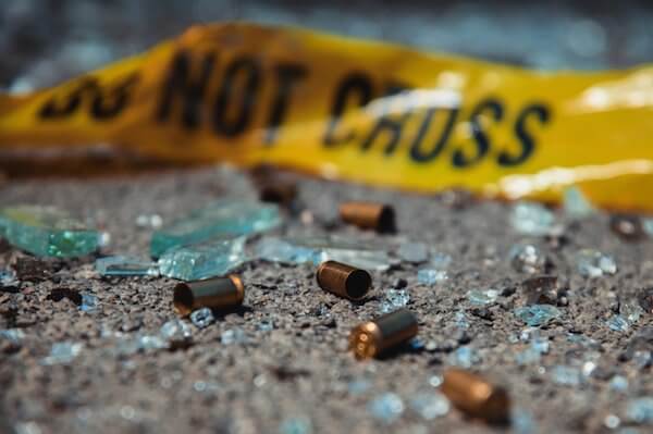 Close-up of bullets and broken glass on the ground, with a yellow "do not cross" sign in the background.
