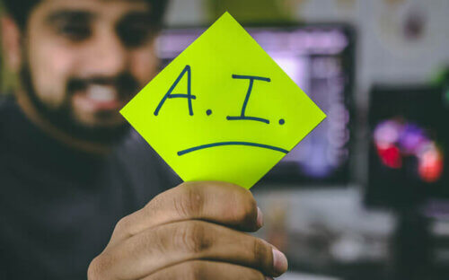 A smiling man holds up an "AI" sign on a green post-it.